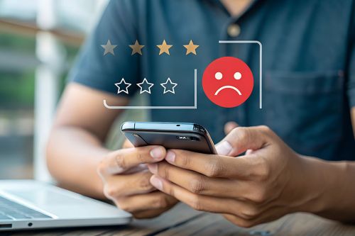 Foto: Mann bedient Smartphone, darüber negatives Smiley und schlechte Sterne Bewertung